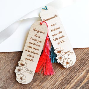 Puede incluir: Dos marcap&aacute;ginas de madera con dise&ntilde;os florales y borlas. Uno dice "Morganne Merci d'avoir pris soin de moi cette ann&eacute;e et de m'avoir aid&eacute; &agrave; grandir." El otro dice "Emmanuelle Merci Ma&icirc;tresse pour cette belle ann&eacute;e de PS."