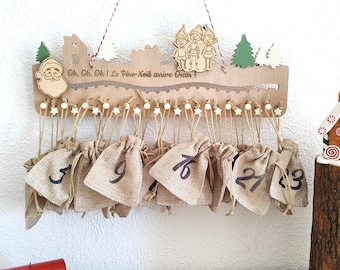 May include: A wooden Christmas advent calendar with 24 small hessian bags hanging from it. The calendar is decorated with a Santa Claus, elves, and a Christmas tree. The text "Oh, Oh, Oh! Le Père Noël arrive Oscar!" is written on the calendar.