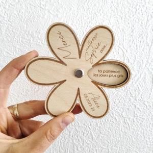 May include: A wooden flower-shaped gift with engraved text. The flower has six petals and a circular indentation in the center. The text includes "Merci", "ma&icirc;tresse Sophie pour...", "ta patience les jours plus gris", "Alice", and "CS 2023-24".