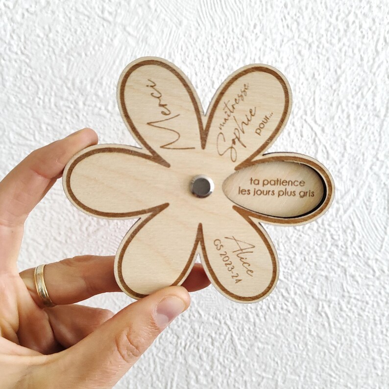 May include: A wooden flower-shaped gift with engraved text. The flower has six petals and a circular indentation in the center. The text includes "Merci", "ma&icirc;tresse Sophie pour...", "ta patience les jours plus gris", "Alice", and "CS 2023-24".
