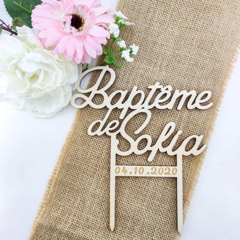 Peut inclure: Topper de g&acirc;teau en bois avec le texte "Bapteme de Sofia" et la date "04.10.2020" en lettres dor&eacute;es. Le topper est sur un fond en toile de jute.