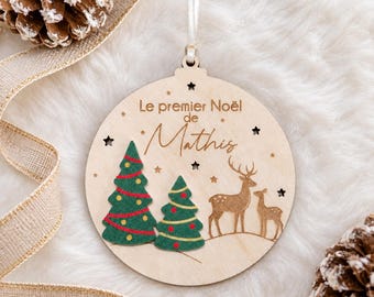 Könnte beinhalten: Ein runder Weihnachtsbaumschmuck aus Holz mit der Gravur Le premier Noël de Mathis, zwei grünen Filztannen mit roten und gelben Akzenten sowie zwei Hirschsilhouetten, aufgehängt an einem weißen Band.