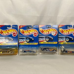 May include: Four Hot Wheels Race Team Series toy cars in their original packaging. The packaging is blue with the Hot Wheels logo and car illustrations. Each car is a different color and design.