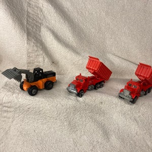 May include: Three toy vehicles, a yellow and black construction vehicle with a scoop, and two red dump trucks with raised beds.