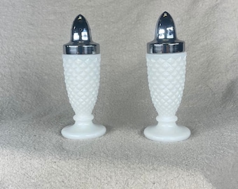 May include: A set of two white salt and pepper shakers with a diamond pattern and silver tops.