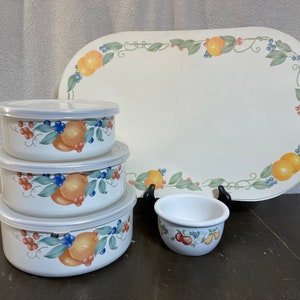 May include: A white ceramic serving set with a fruit design. The set includes three round bowls with lids, a small bowl, and an oval serving platter. The fruit design features oranges, blueberries, and green leaves.
