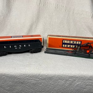 May include: A vintage Lionel Electric Train set with a black boxcar, track, and a control unit with a red button. The boxcar has the text "Lionel 60 32" printed on it.