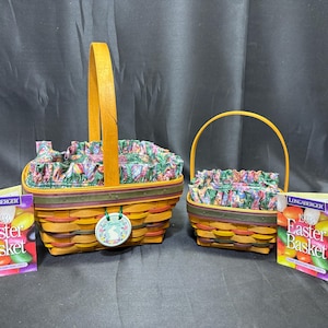 May include: Two Longaberger Easter baskets with floral fabric liners and wooden handles. The baskets are woven in shades of brown and yellow. Two accompanying cards read "1999 Easter Basket".