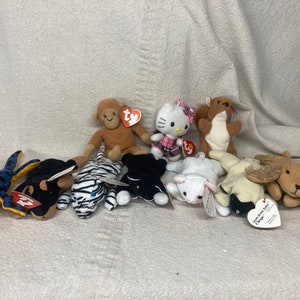 以下が含まれることがあります： 茶色の猿、ハローキティ、リス、白いウサギ、黒い犬、青と黒のトカゲ、白と黒のトラ、茶色のヘラジカなど、Ty Beanie Babiesのぬいぐるみコレクション。各おもちゃにはTyのハート型のタグが付いています。