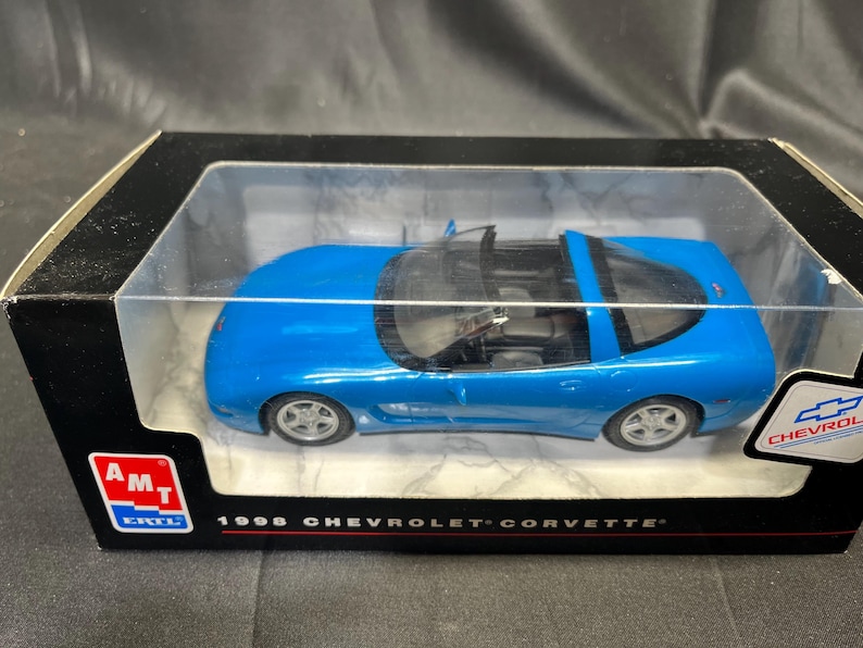 Puede incluir: Un coche modelo azul de un Chevrolet Corvette de 1996 en una caja de presentaci&oacute;n. El coche modelo es de un azul vibrante con ruedas plateadas y un interior negro. La caja tiene el logotipo de Chevrolet y el texto "1996 Chevrolet Corvette".