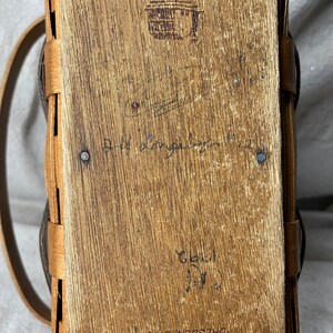 May include: A Longaberger Basket with a brown leather handle and a wooden base. The basket is stamped with the words "Longaberger Baskets, Handwoven, Dresden, Ohio, USA".