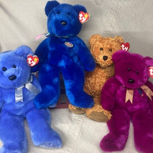 Puede incluir: Cuatro osos de peluche con etiquetas Ty. Los osos son azules, morados, marrones y azules. Los osos azules tienen cintas plateadas alrededor del cuello. El oso morado tiene una cinta dorada alrededor del cuello.