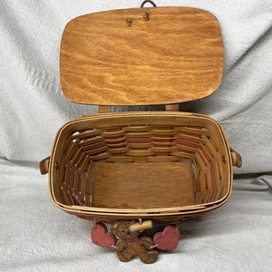 May include: A wooden basket with a hinged lid and a woven design. The basket is decorated with pink hearts and a small wooden bear figurine.
