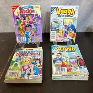Puede incluir: Cuatro cómics con Archie y sus amigos. Los cómics están apilados sobre una superficie de madera. Los cómics se titulan "World of Archie Double Digest", "Laugh Digest Magazine", "Archie's Pals'n Gals Double Digest" y "Laugh Digest Magazine".
