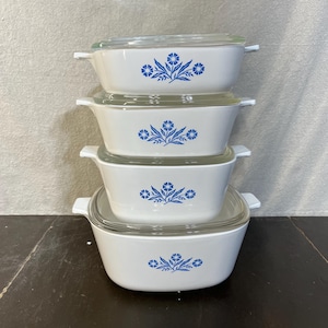 May include: A set of four white casserole dishes with blue floral designs. The dishes are stacked on top of each other.