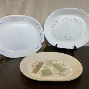 May include: Three white oval ceramic serving platters with different floral designs. The platters are on a brown surface.