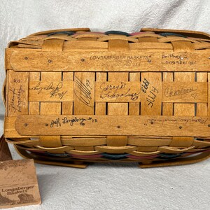 May include: A Longaberger basket with a red, white, and blue woven design. The basket is signed by Jeff Longaberger and several other people. The basket has a tag that says "Longaberger Baskets".