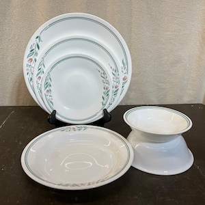 May include: Set of four white ceramic plates with a green and pink floral design. The plates are nested together and include a bowl.