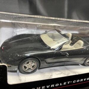 Puede incluir: Un coche modelo descapotable negro con asientos interiores color crema. El coche est&aacute; en una vitrina de pl&aacute;stico transparente. Las ruedas tienen llantas plateadas. Es un Chevrolet Corvette.