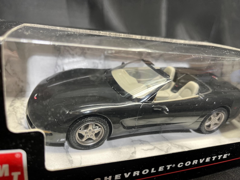 Puede incluir: Un coche modelo descapotable negro con asientos interiores color crema. El coche est&aacute; en una vitrina de pl&aacute;stico transparente. Las ruedas tienen llantas plateadas. Es un Chevrolet Corvette.