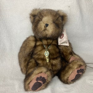 Puede incluir: Un oso de peluche marrón con una llave en un collar. El oso tiene una etiqueta que dice "The Hand-Made Bear Collection".