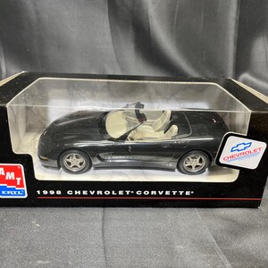 Puede incluir: Un modelo de coche negro de un Chevrolet Corvette de 1998 en una caja de presentaci&oacute;n. El modelo tiene un interior beige y ruedas plateadas. La caja tiene el logotipo de Chevrolet y el texto "1998 Chevrolet Corvette".