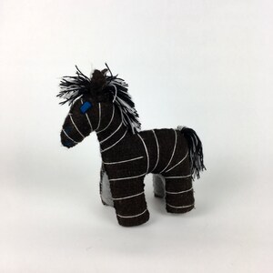 Op de afbeelding: Een bruin en wit gestreept knuffelzebra met blauwe ogen. De zebra staat op een wit oppervlak.
