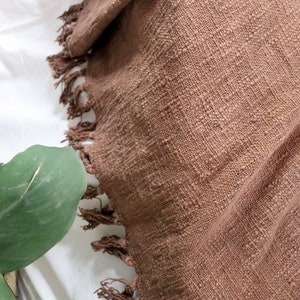 May include: A brown throw blanket with a fringed edge. The blanket is made of a soft, textured fabric.