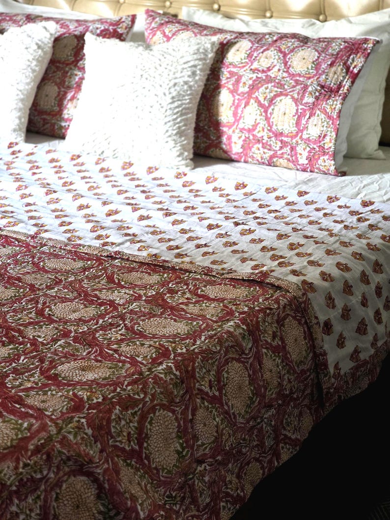 May include: A bed is made with a white and red floral patterned quilt and matching decorative pillows. The pillows are white and red with a floral design. The bed has a white headboard and white sheets.