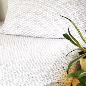 May include: White bed linen with a small brown floral pattern. A green plant is in the corner of the bed.