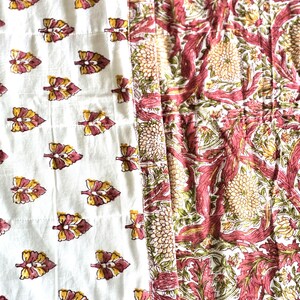 May include: A quilted textile featuring two distinct patterns. One side showcases a white background with repeating leaf motifs in yellow and maroon. The other side displays a floral design in maroon, green, and yellow.