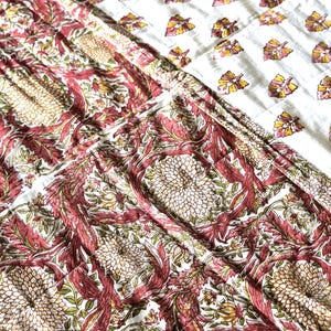 May include: A close-up of a white and red floral patterned quilt. The quilt features a repeating pattern of large, stylized flowers and leaves in shades of red, pink, and green. The top section has a white background with a repeating pattern of yellow and pink leaves.