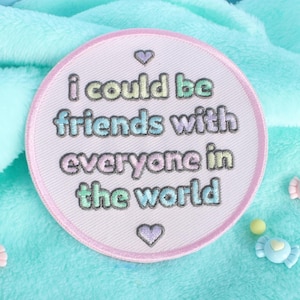 May include: A white embroidered patch with a pink border. The patch has a heart at the top and bottom and says "i could be friends with everyone in the world".