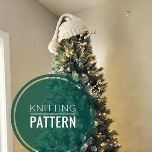 May include: A green Christmas tree decorated with white lights, gold ornaments, and a white knitted stocking hat. The tree is sitting on a brown wicker tree skirt. The text "Knitting Pattern" is written in a circle on the tree.