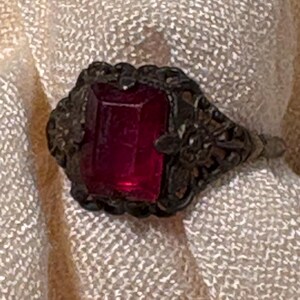 Anillo vintage de cristal rojo rubí de los años 60, talla 5, con intrincado diseño de filigrana y acabado en tono plateado.