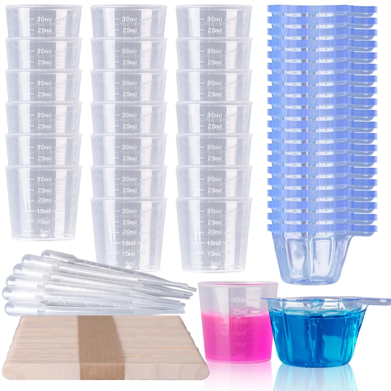 May include: A set of 24 clear plastic measuring cups with blue markings, ranging in size from 5 ml to 30 ml. The set also includes a wooden stirring stick, two droppers, and two small cups filled with pink and blue liquid.