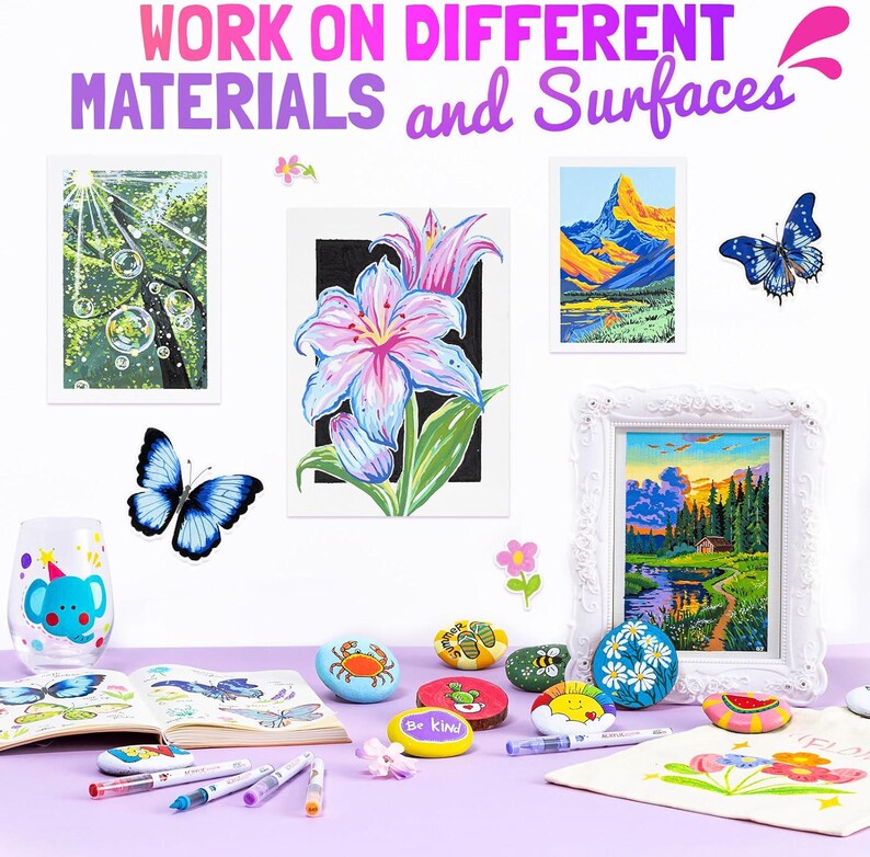 May include: An assortment of painted rocks, framed artwork, and a decorated glass are displayed on a purple surface. The artwork includes a landscape, a flower, and a tree scene. The text at the top reads "WORK ON DIFFERENT MATERIALS and Surfaces."