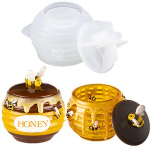 May include: A collection of bee-themed honey pots and molds. The pots are yellow and brown with honey dripping down the sides, and feature bee figurines. One pot has the word "HONEY" on it. The molds are white and designed to create the honey pots.