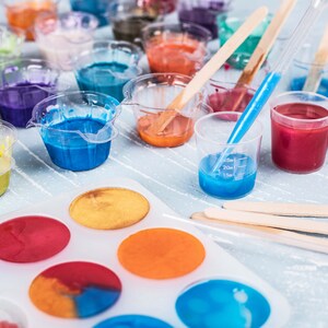 May include: A white plastic mold with eight round cavities for making resin crafts. The cavities are filled with colorful resin, including blue, orange, yellow, and red. There are also several small cups filled with different colored resin, including blue, red, orange, and yellow.
