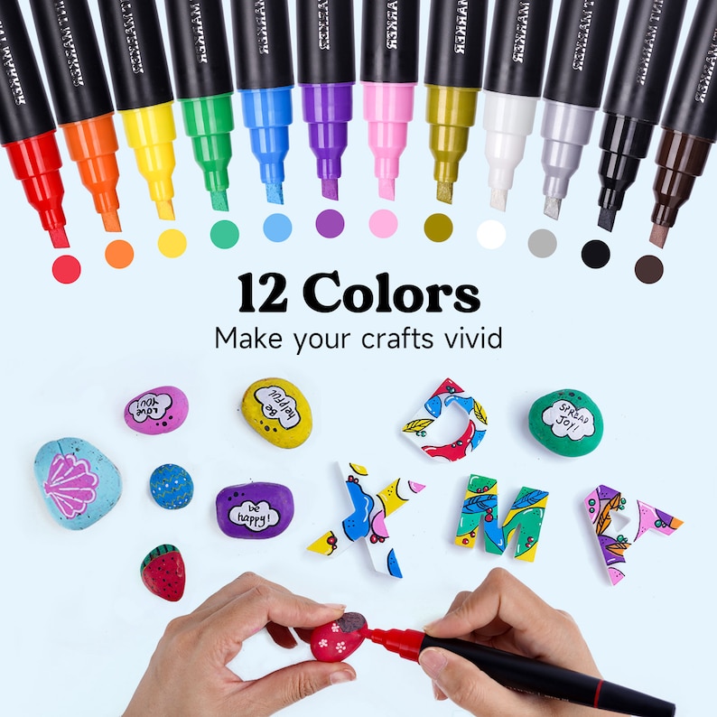 May include: Set of 12 paint markers with black caps and colorful paint tips. The markers are arranged in a row with the tips facing the viewer. The colors are red, orange, yellow, green, blue, purple, pink, gold, white, gray, black, and brown. The text "12 Colors" and "Make your crafts vivid" is displayed below the markers. The image also shows painted rocks and letters.