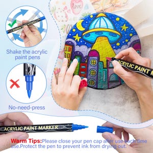 May include: A set of black acrylic paint markers with white lettering that says "Acrylic Paint Marker Fine". The markers have blue tips and are shown being used to color a round canvas with a drawing of a city and a UFO. The image includes instructions to shake the markers before use and to close the cap after use to prevent the ink from drying out.