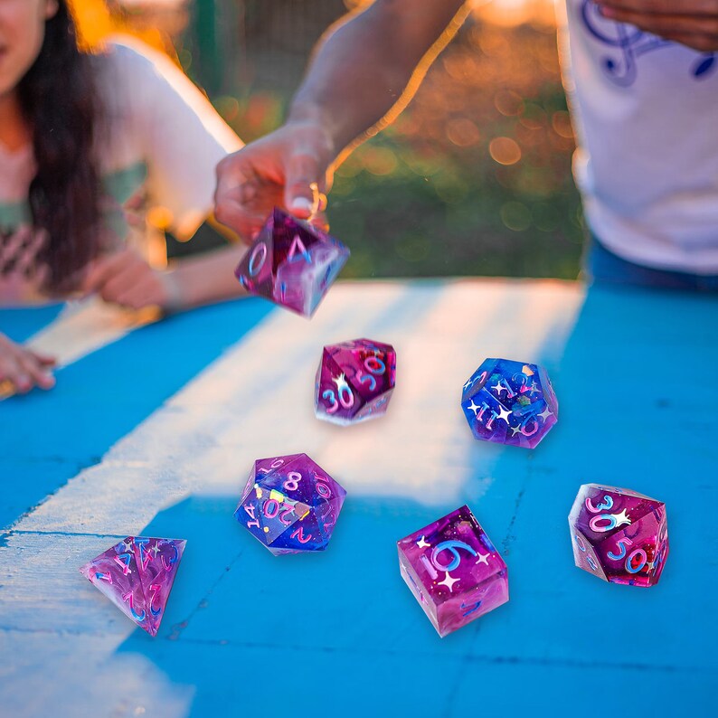May include: A set of six iridescent dice with pink, blue, and purple glitter embedded in the clear plastic. The dice are on a blue surface with white lines.