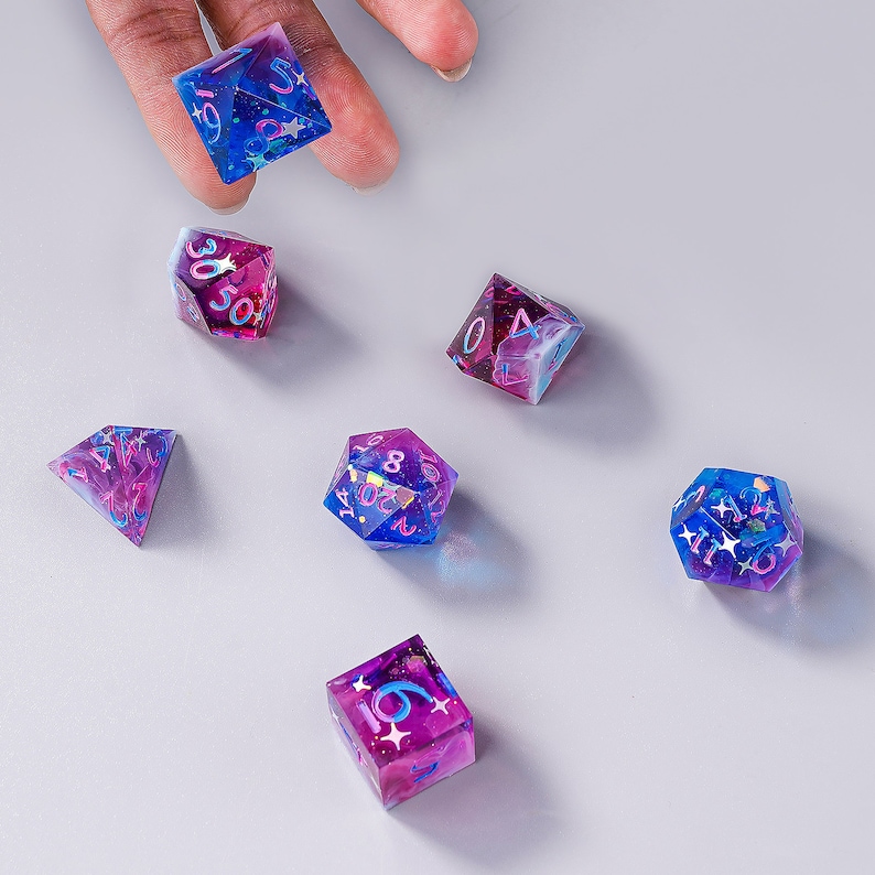May include: A set of six iridescent dice with pink and blue swirls and glitter. The dice are numbered 1 through 6 and have a star design on each face.