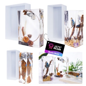 May include: Four clear rectangular resin molds with different floral and butterfly designs. The molds are made of silicone and are designed for creating resin crafts. The molds are shown on a white background with a tag that says "Let's Resin Resin Mold".