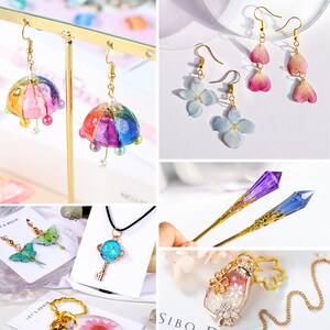 May include: Assortment of handmade resin jewelry featuring various designs, including a colorful umbrella, pressed flowers, a key with a planet charm, a bottle with glitter and snowflakes, and a crystal-shaped hair stick.