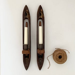 May include: Two wooden candle holders with a spindle design, each with a white candle inside. A ball of twine is in the lower right corner of the image.