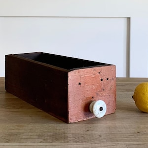 May include: A dark brown wooden box with a white knob on the side. The box is sitting on a wooden surface.
