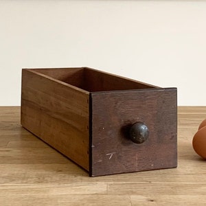 May include: A wooden drawer with a dark brown finish and a black metal knob. The drawer is sitting on a wooden surface.