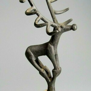May include: A bronze sculpture of a stylized deer with large antlers, standing on a white marble base.