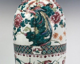 May include: A white porcelain vase with a green, blue, and pink floral design. The vase has two handles in the shape of dragons. The vase is decorated with a phoenix and other birds.